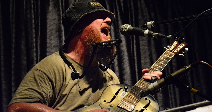 Big Joe Bone playing the guitar and harmonica onstage.
