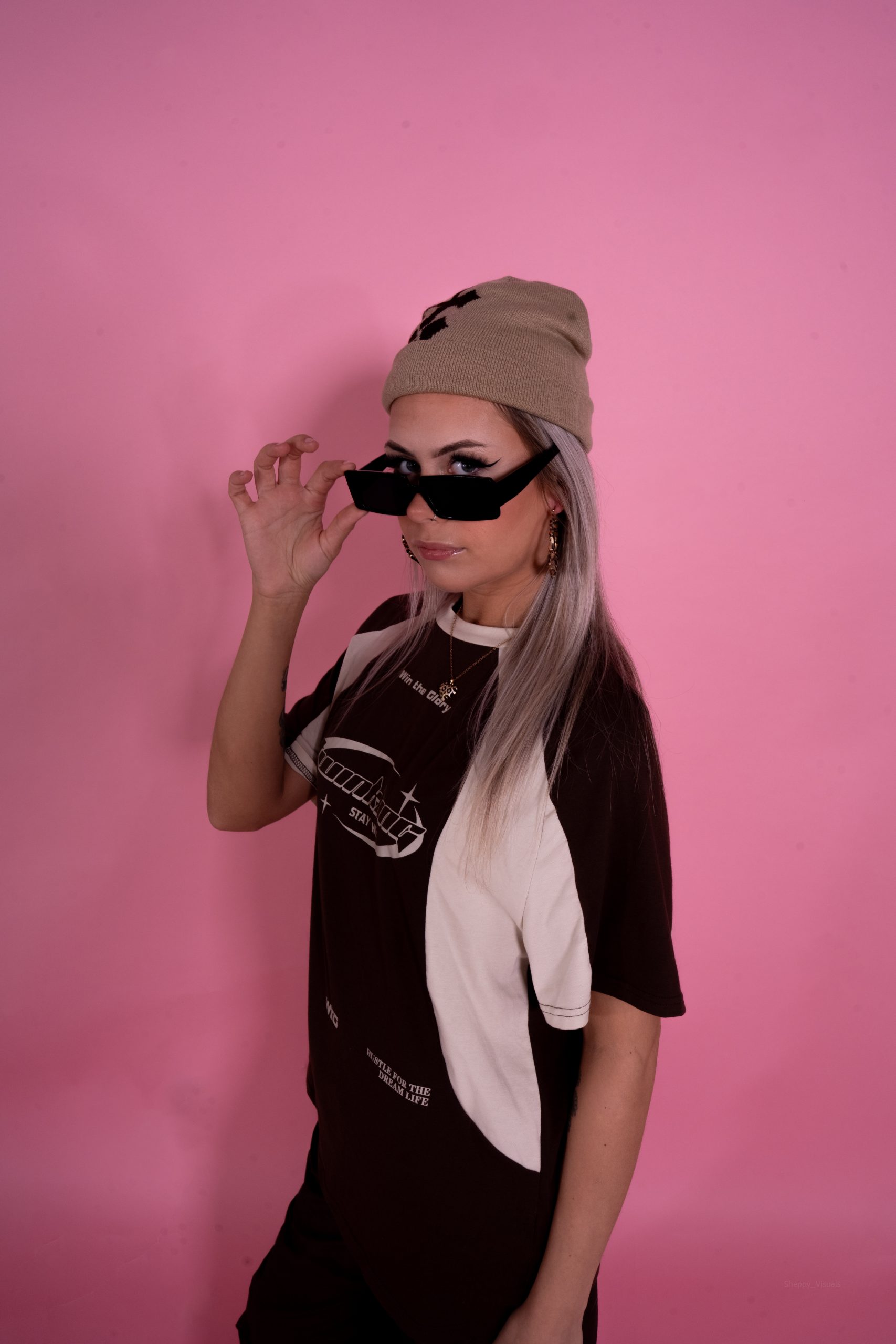 Geometrikk stood in front of a pink wall with sunglasses and a hat on.
