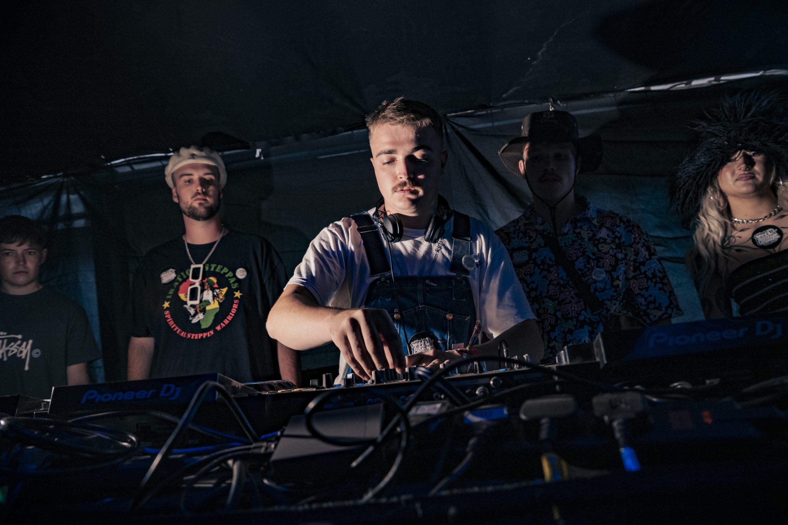 4 men and 1 women stood behind dj mixers